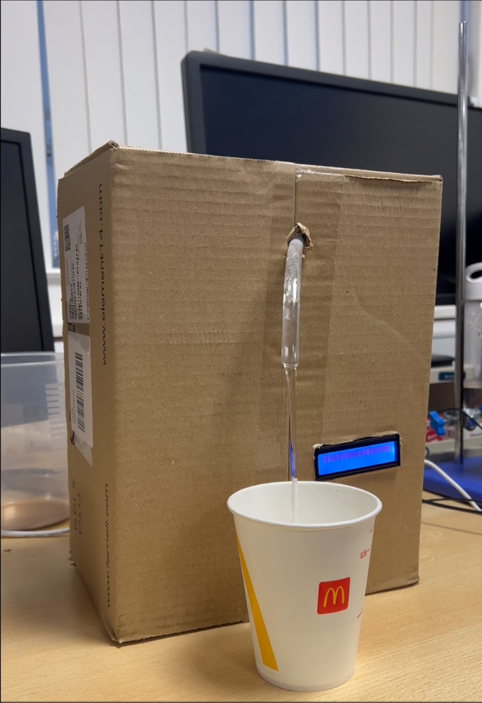 Early Aquaflow demo dispensing into a McDonald's cup from a cardboard enclosure